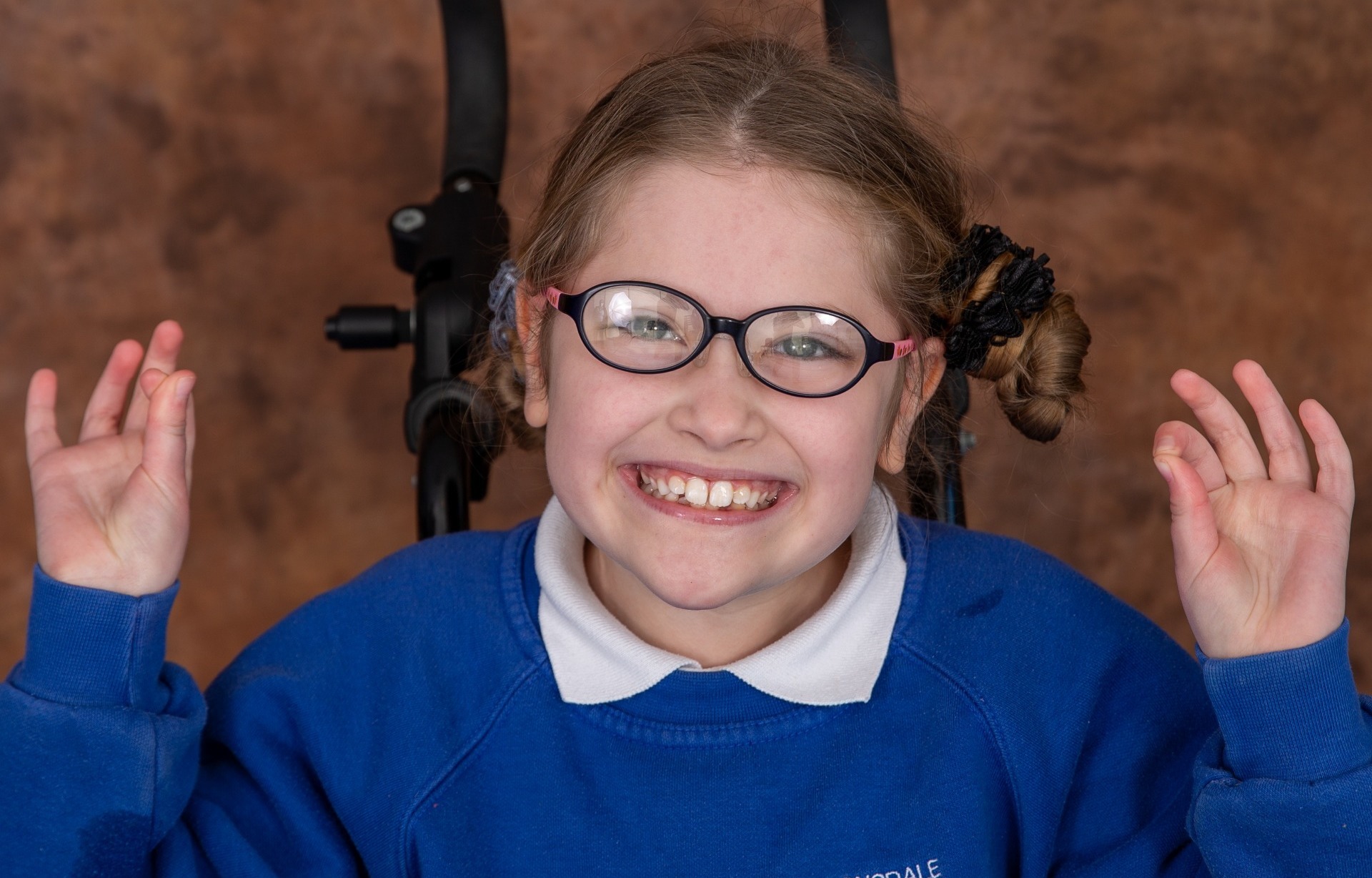 Young white girl in her wheelchair giving two ok signs in her school uniform for her school photograph