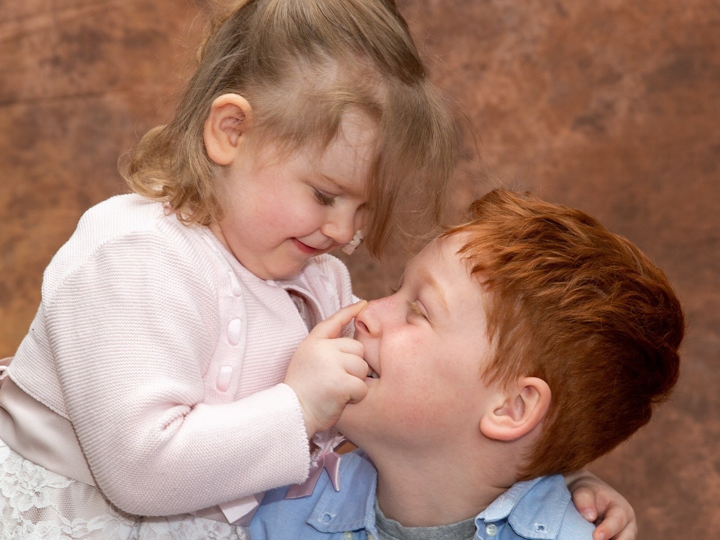 A toddler girl with medical condition posing for a photograph with her older brother at a Hospice